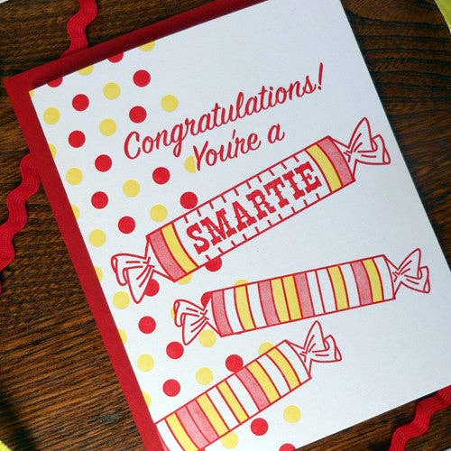 Card with candy illustrations and 'Congratulations! You're a SMARTIE' text on a wooden surface