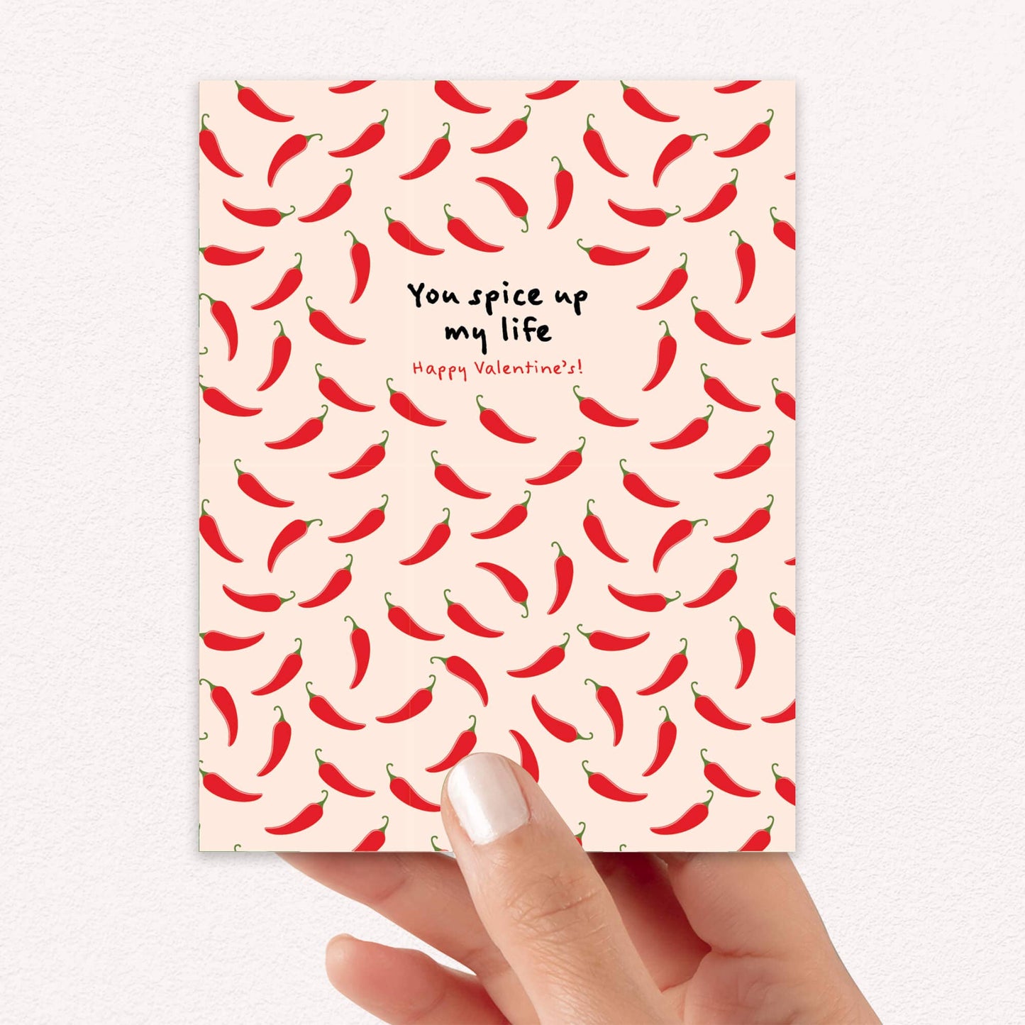 Card with red chili pepper pattern and text on a light pink background, held by a hand.