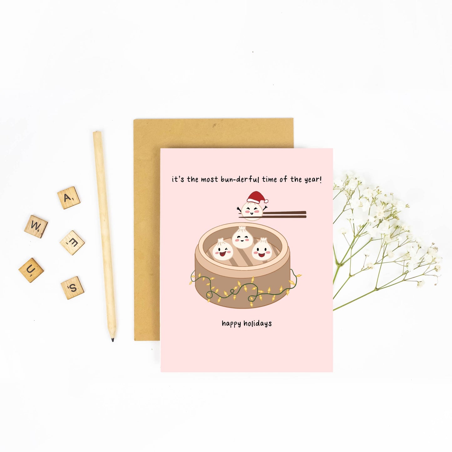 holiday greeting card with 4 steamed buns in a bamboo steamer. One is wearing a santa hat and there are string lights along the bottom of the steamer.