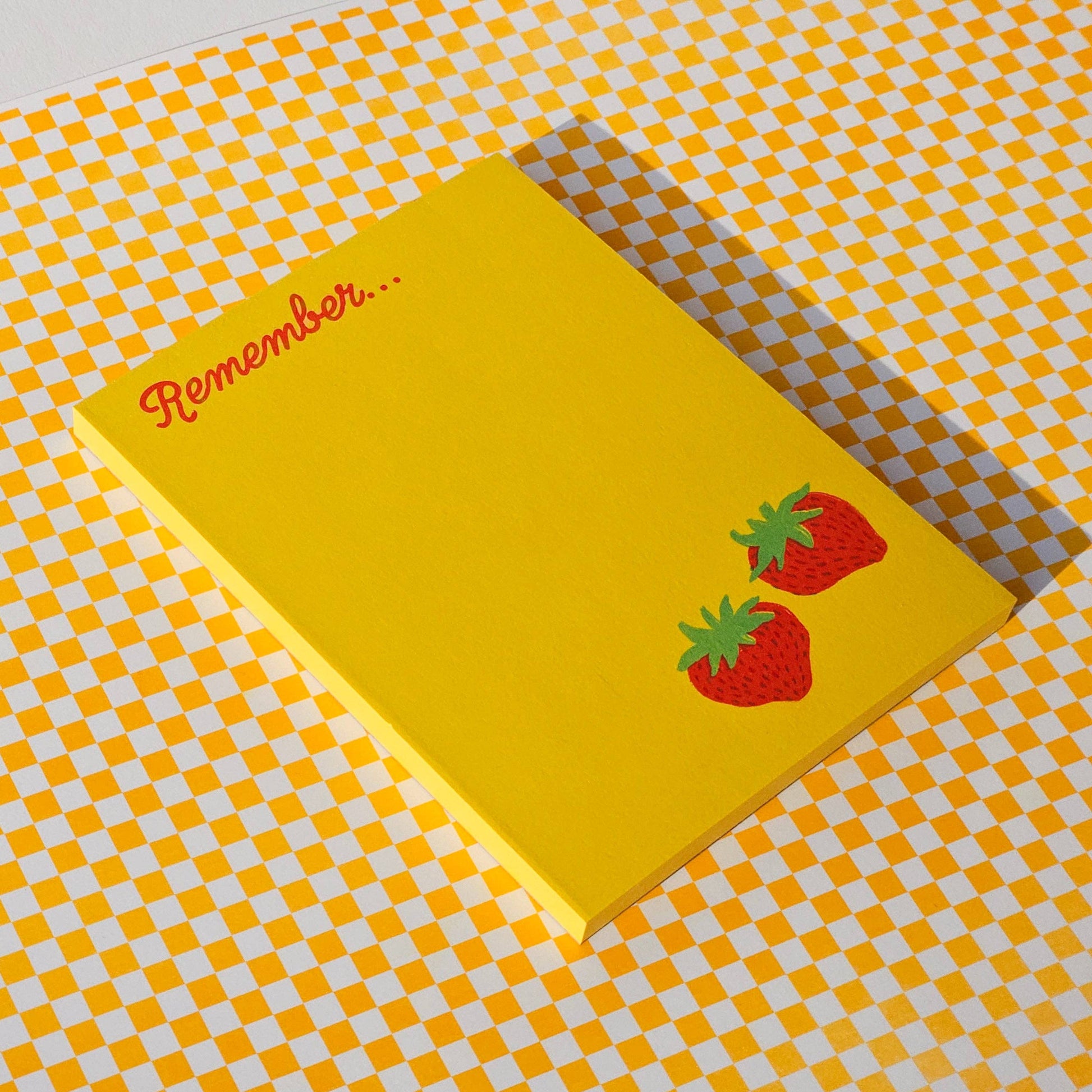 Yellow notepad on yellow and white checkerboard background. Notepad has two red strawberries in bottom right corner, top let reads "Remember..."