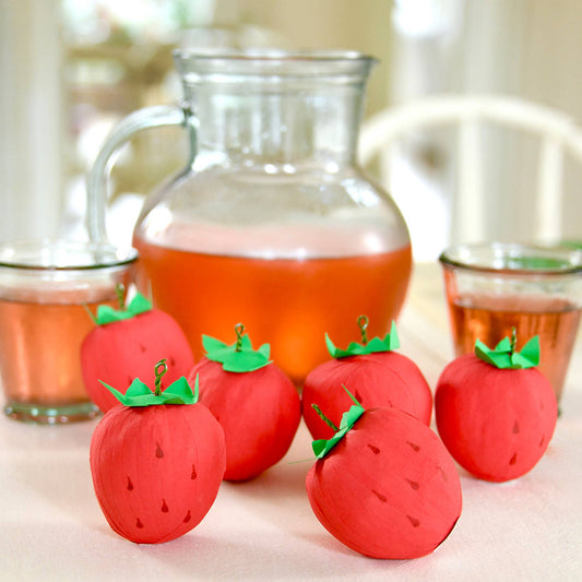 Crepe paper wrapped surprise balls made to look like a strawberries. Pictured here on table with a pitcher and filled glasses of iced tea