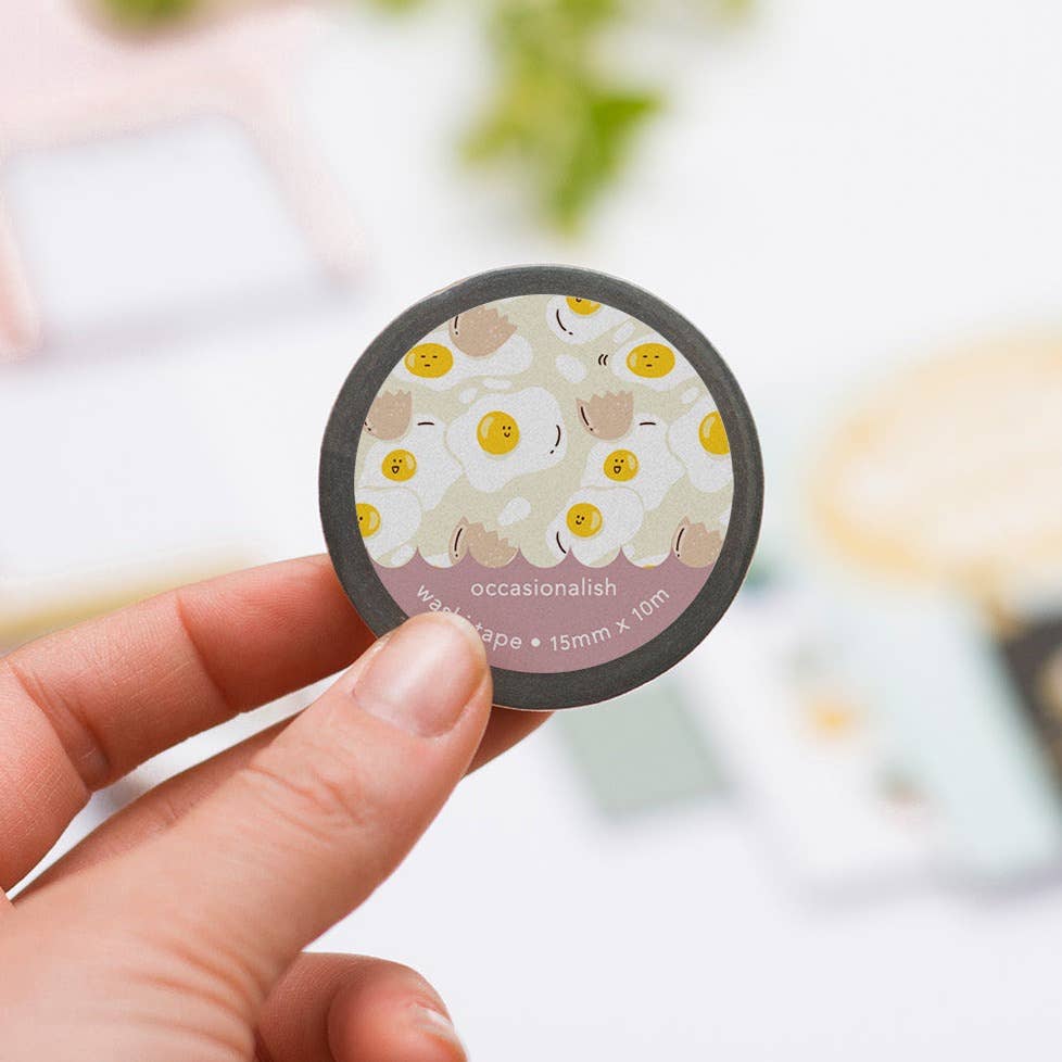 Sunny side up washi tape with assorted eggs and cracked egg shells. Hand holding up a roll of tape.