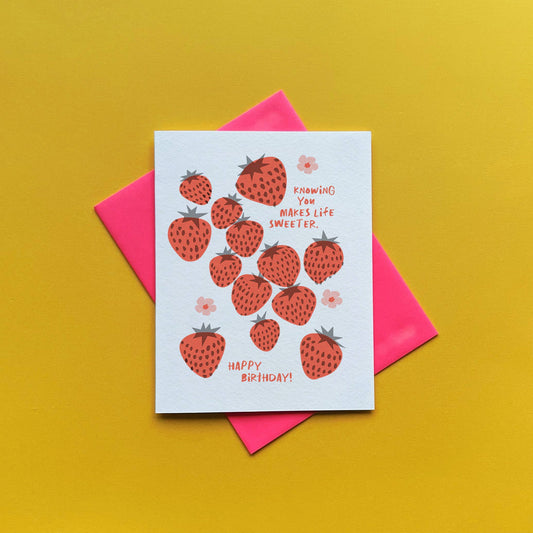 Greeting card -- mostly white with red strawberries and pink flowers all over. text reads "Knowing you makes life sweeter. Happy birthday!"
