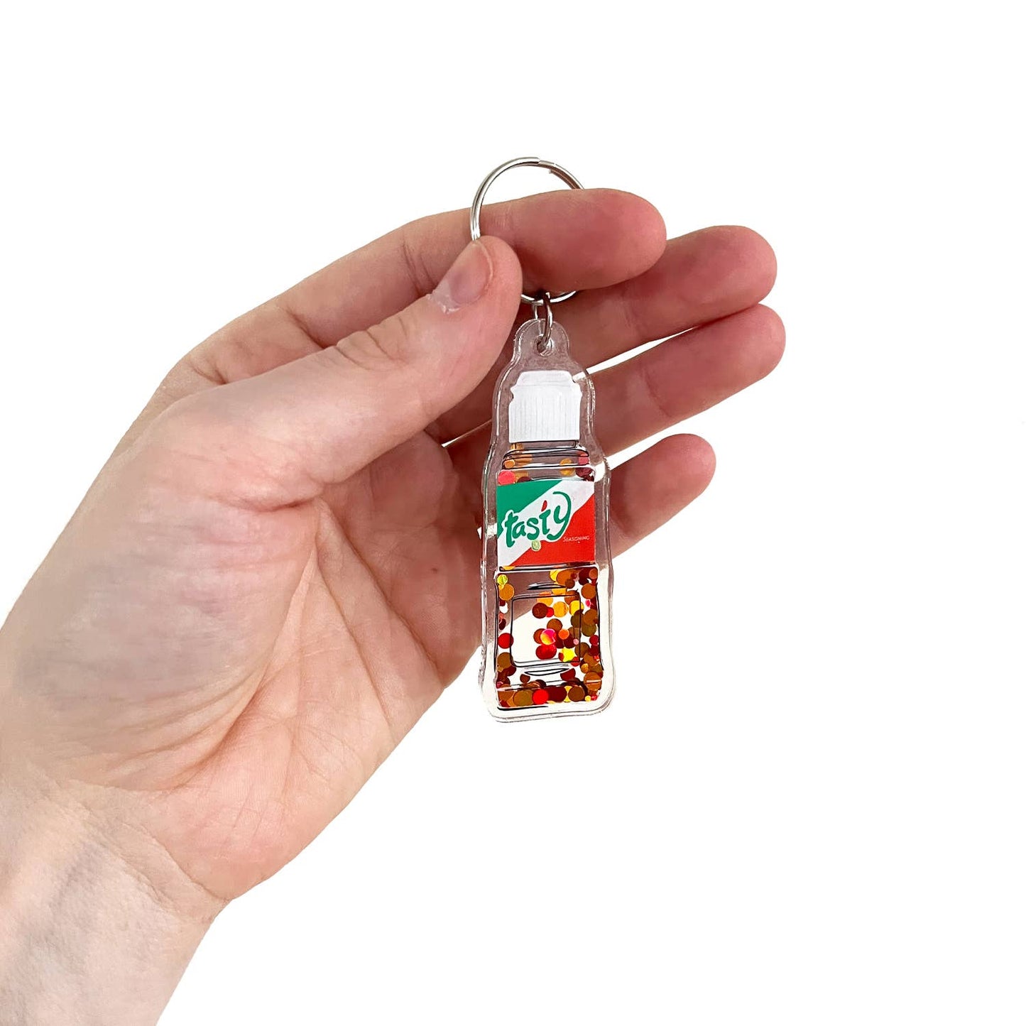 tajin bottle keychain that has floating glitter pieces to mimic the seasoning powder and it reads "tasty"