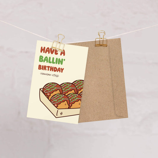 Birthday card with takoyaki illustration and humorous text "Have a ballin' birthday (takoyaki style)" on a beige background