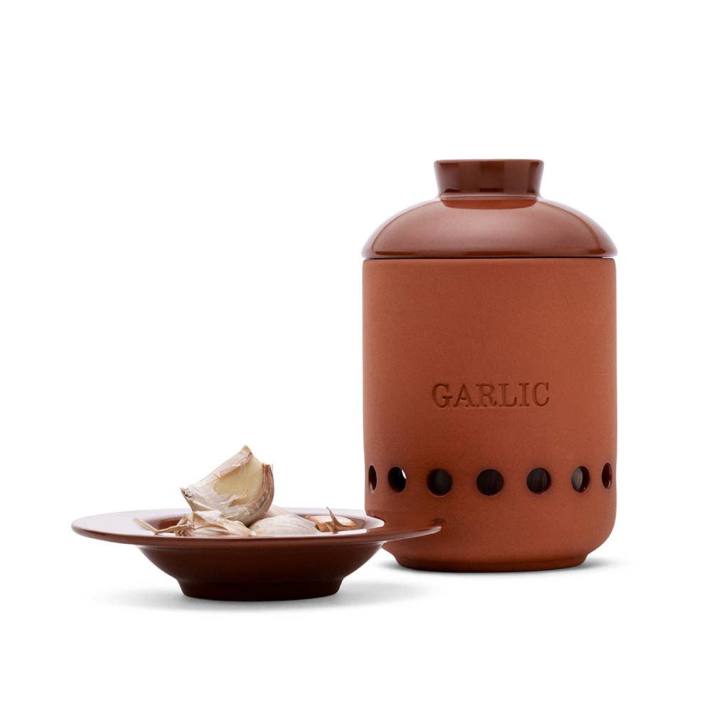 Terracotta garlic storage jar with a small dish of garlic cloves on a white background