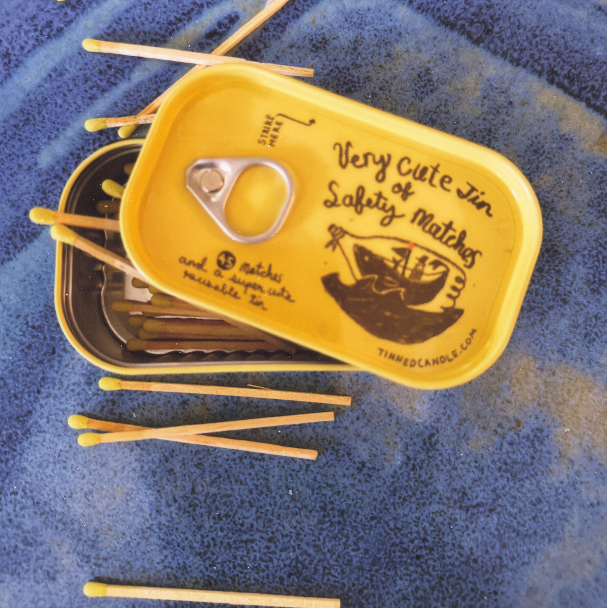 Yellow match tin with safety matches on a blue textured surface