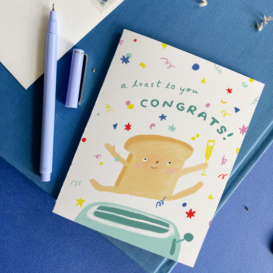 Greeting card with a toast character popping out of a toaster and 'a toast to you, Congrats!' text on a blue background