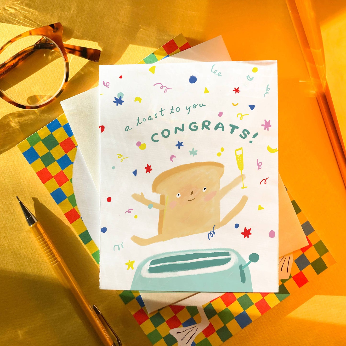 Greeting card with a toast character popping out of a toaster and 'a toast to you, Congrats!' text on a colorful background