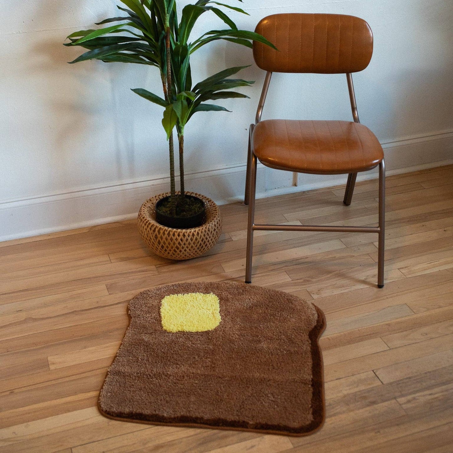 toast shaped rug with a pad of butter on it. Rug is photographed on floor in front of a plant and chair