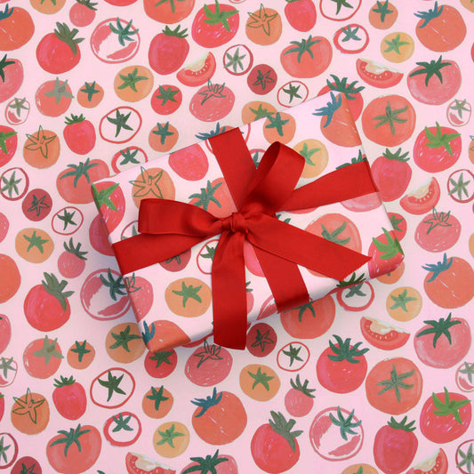sheet of gift wrap with tomatoes all over it. On top of the sheet is a gift wrapped with the tomatoes gift wrap with a red bow
