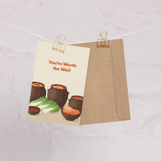 Greeting card with illustrations of Korean clay pot jars and cabbage with text that reads 'You're Worth the Wait' on a beige background.