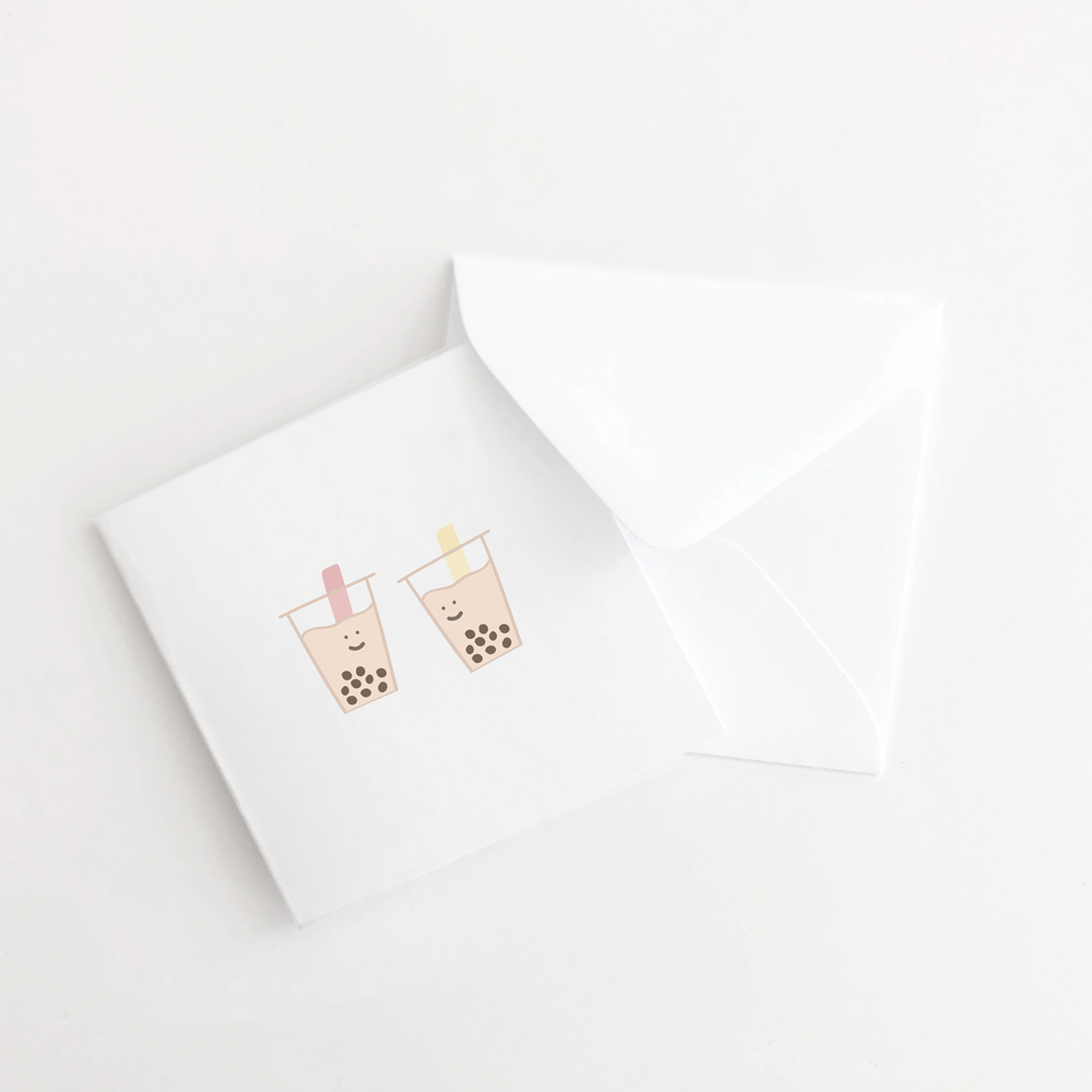 White mini greeting card with white envelope. On the front of the card are two boba cups smiling at each other.