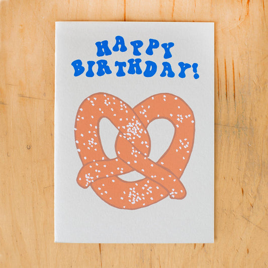 Photo of greeting card with blue text in bubbly font "Happy Birthday!" and image of large salty pretzel.