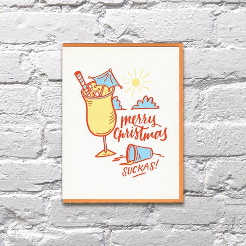 Christmas greeting card that reads "Merry Christmas, Suckas!" and has an illustration of a tropical drink with cocktail umbrella, used shot glass and sunshine on it.