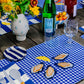 Table setting featuring a blue gingham placemat with four oysters on the half shell and a lemon wedge embroidered in the center 
