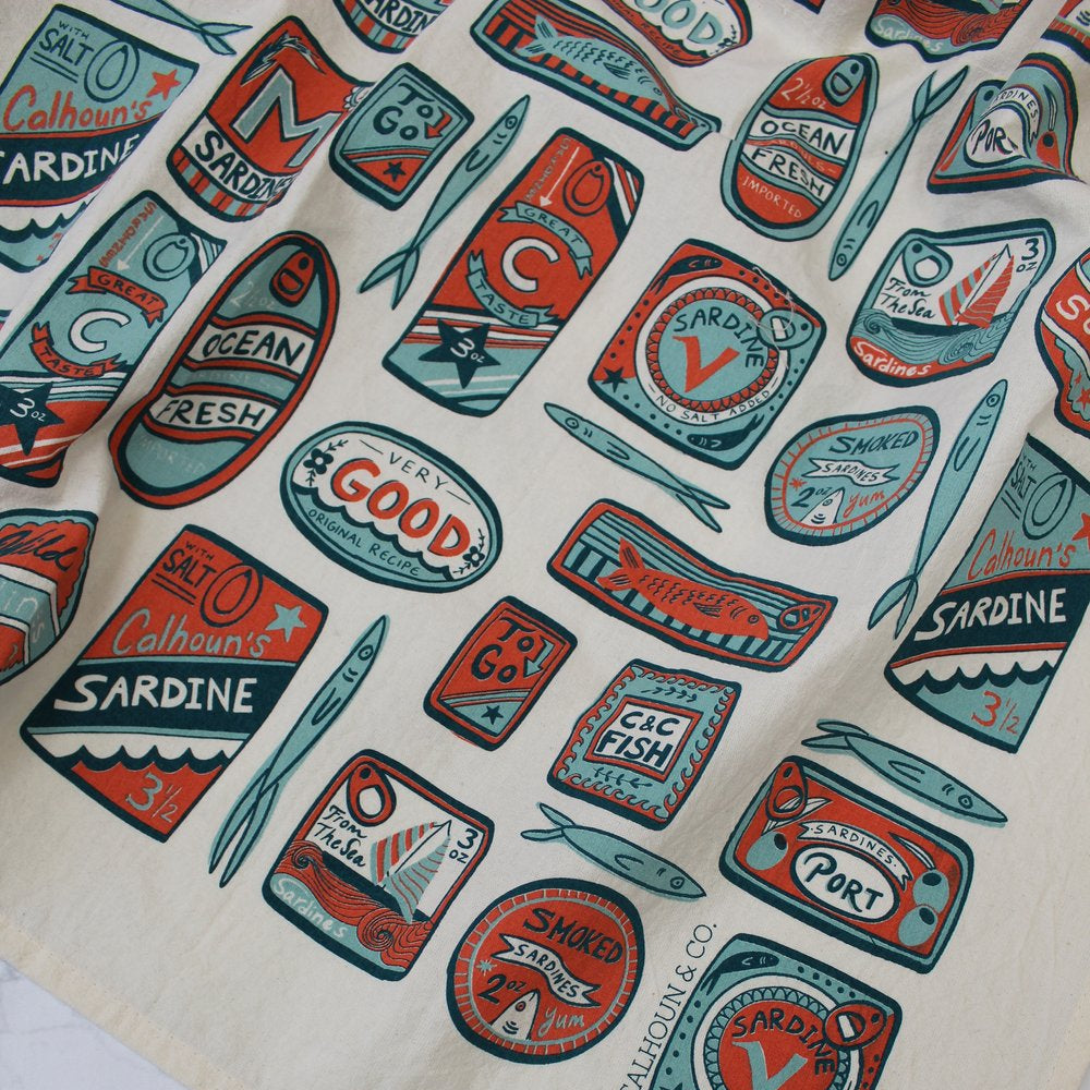 Close up view --- white tea towel with various shaped sardine tin cans in a red, light blue and navy colorway