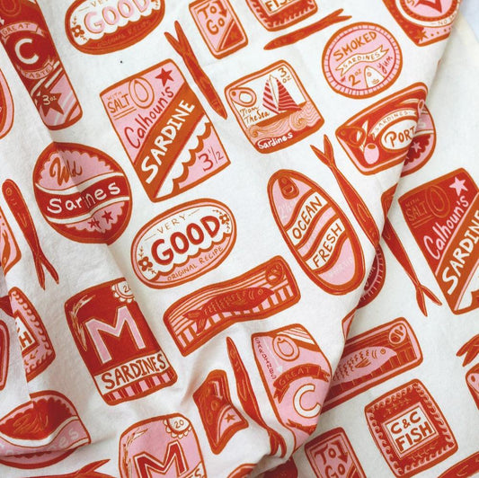 Close up view -- white tea towel with variously shaped sardine tin cans that are red and pink