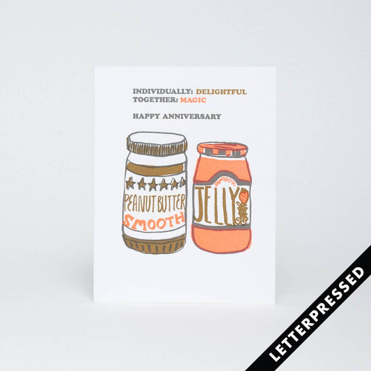 Greeting card that has images of a jar of smooth peanut butter and a jar of strawberry jelly on it. Up top it reads "Individually: delightful. Together: magic. Happy Anniversary" 