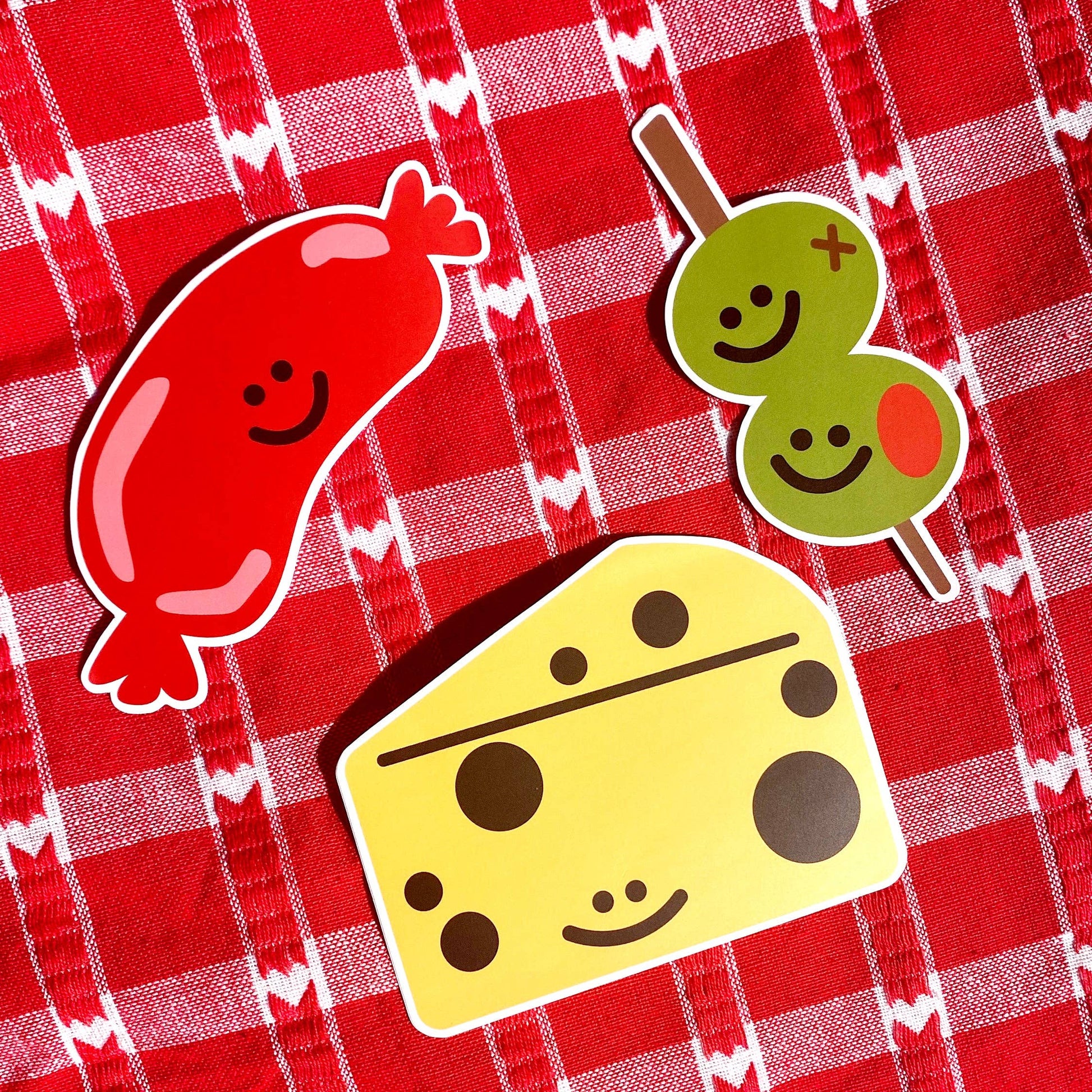 Stickers: Sausage, cheese and olives on a stick. Laying on top of a red and white table cloth.