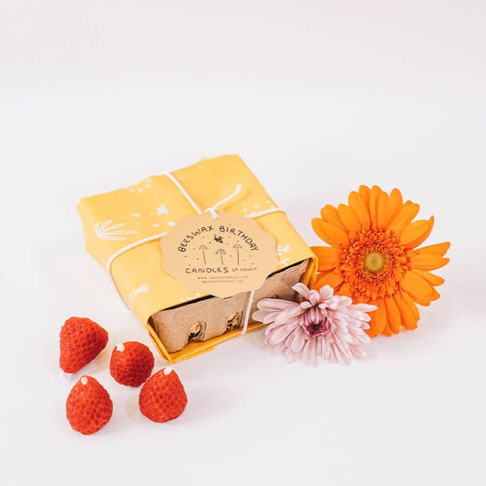 Beeswax birthday candles in a fruit crate wrapped with twine. 4 candles out of the box. 2 gerber daisies next to the box.