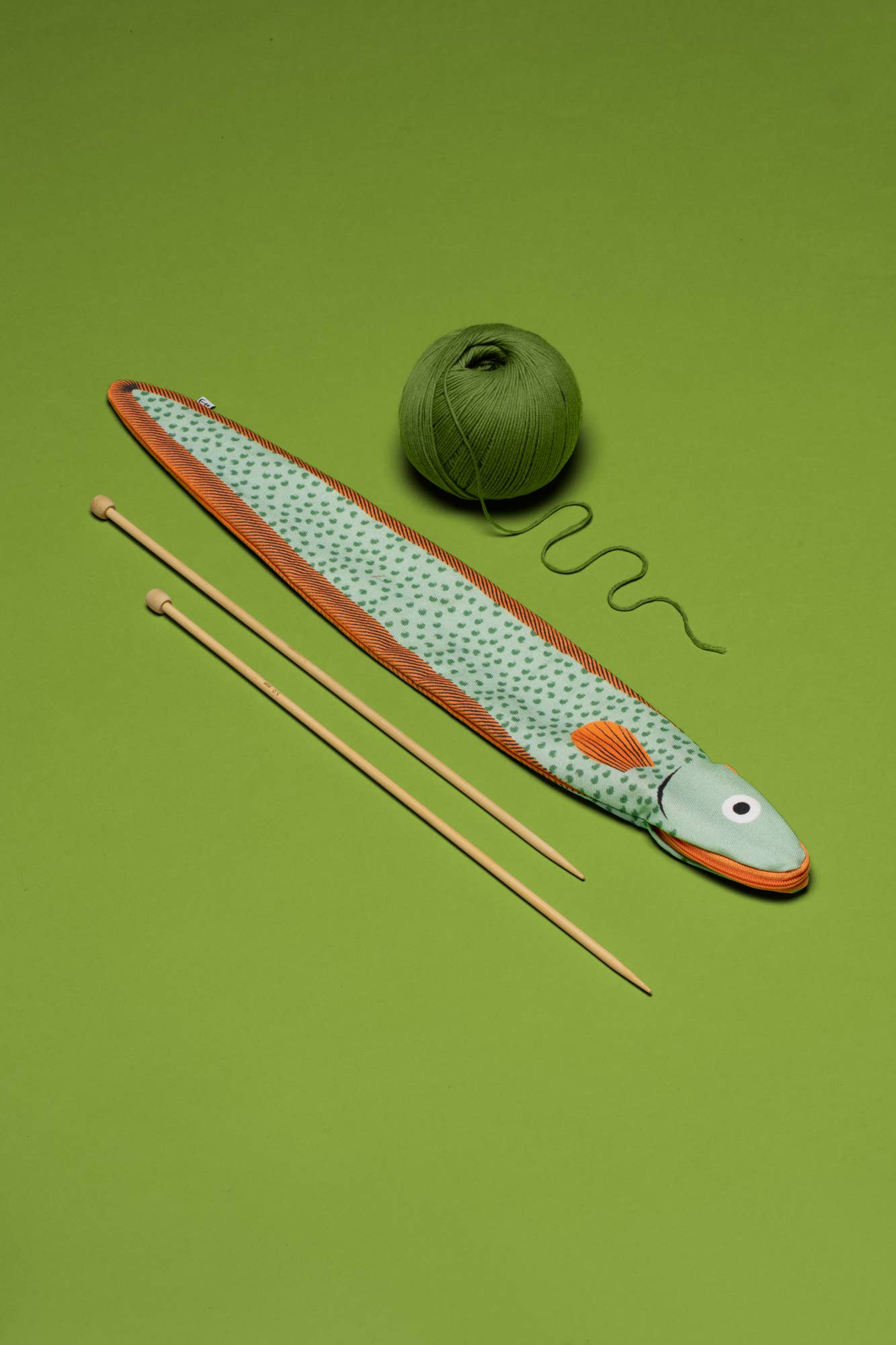 Flat lay of eel pouch next to knitting needles and yarn 