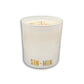 A white glass candle jar with the name 'SIN-MIN' printed in gold at the bottom, filled with white wax and topped with a light brown spice dusting, shown on a white background.