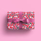 Gift wrapped in pink gift wrap with red cherries and white flowers on it. Bow is pink as well. 