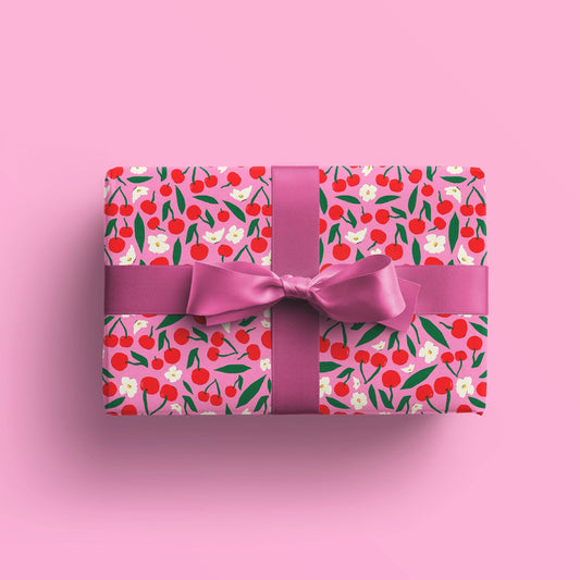 Gift wrapped in pink gift wrap with red cherries and white flowers on it. Bow is pink as well. 