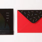 Photo showing front of matchbook greeting card - black with subtle flame design and text "You Two Are." Next to the card is a red envelope (shown from behind) with black flap and rainbow colored matches printed onto flap.