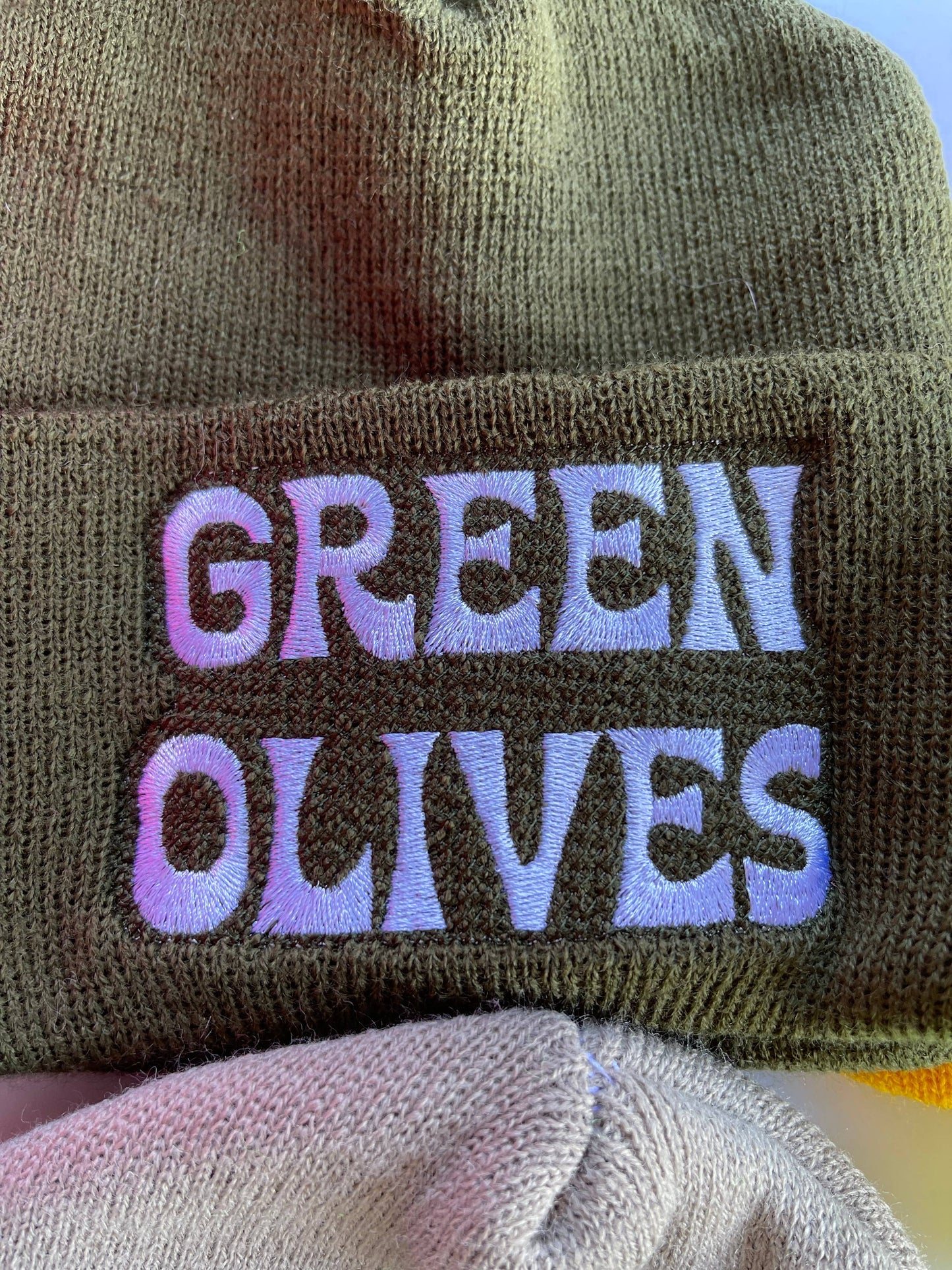 close up of white embroidered text that reads "Green Olives" on olive green beanie 