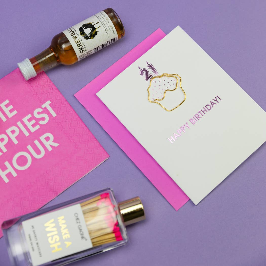 A personal bottle of alcohol, a napkin with text, and a birthday card on a purple background.