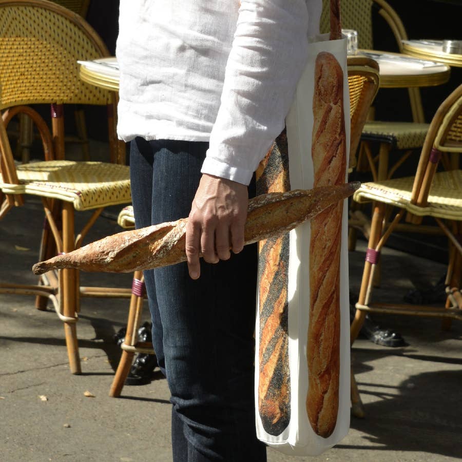 close up of person holding a baguette with a baguette bag on there shoulder 