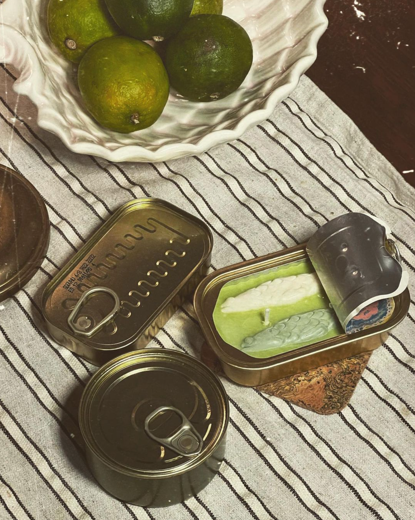 Opened tinned fish candle next to two closed tin cans 