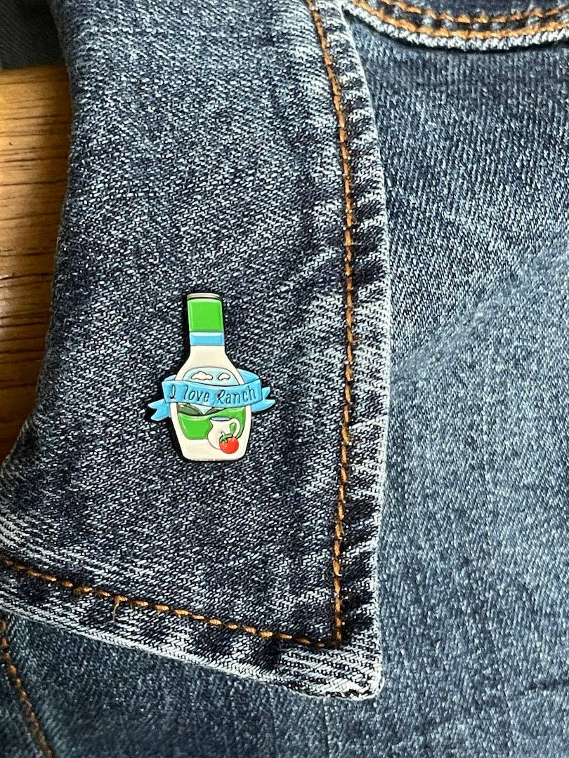 Ranch bottle lapel pin that has a ribbon across the bottle that says "I love Ranch" pinned on a jean jacket's lapel.
