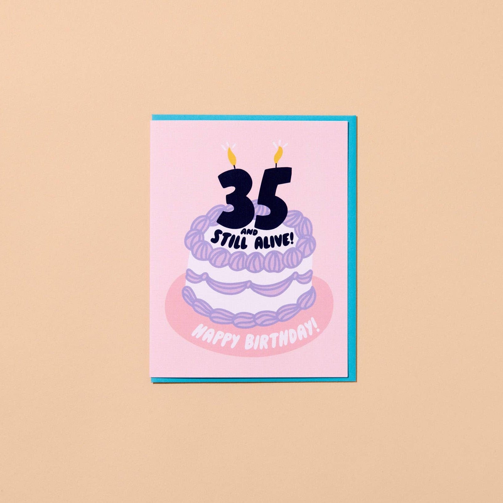 A square birthday card with a pink front and turquoise border, featuring a stylized purple cake with the text '35 Still Alive!' and 'Happy Birthday!' on a warm beige background.