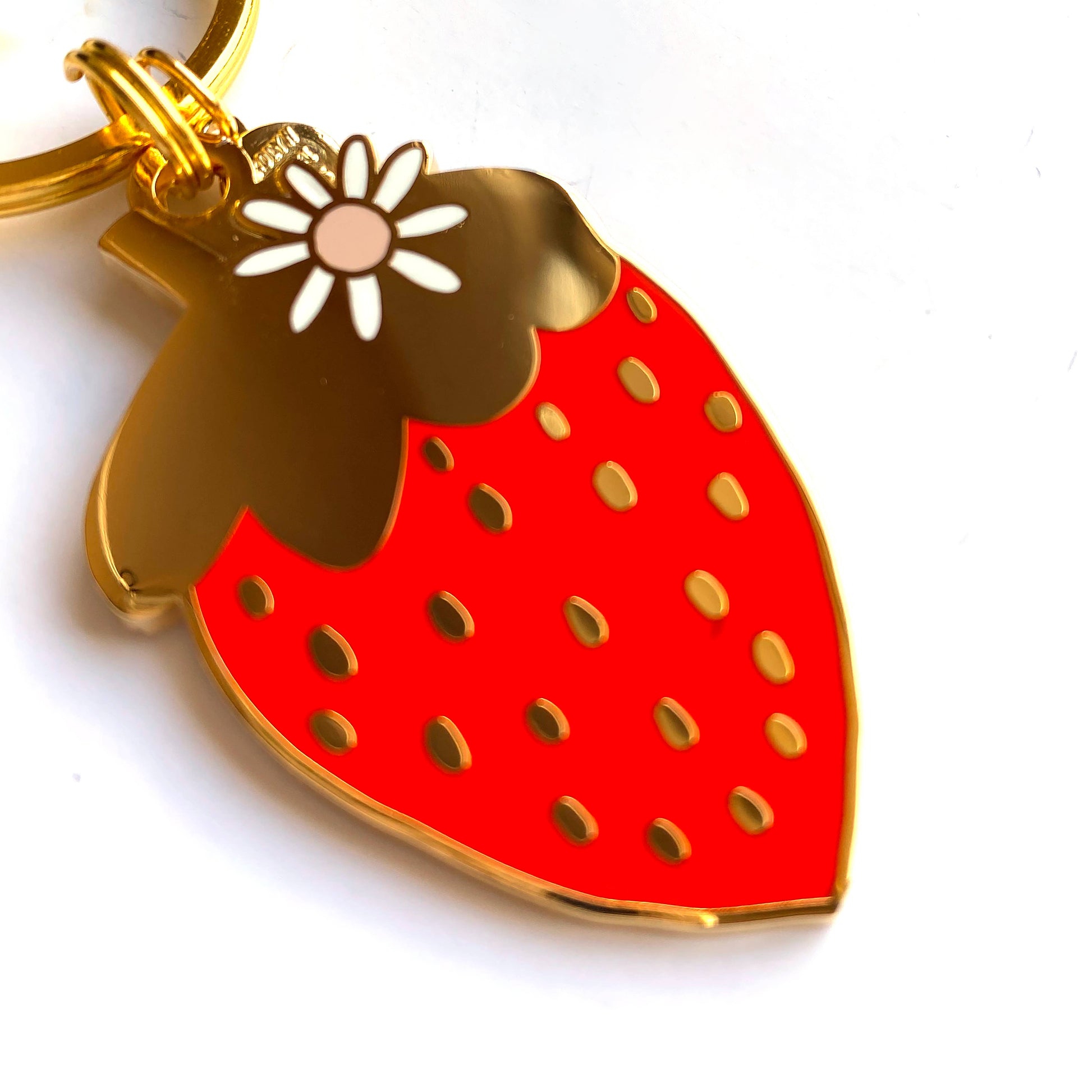 Close up of gold, hard enamel strawberry keychain.