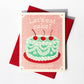 Birthday card with green frilly cake, decorated with ribboned icing and three red cherries on the top. Text reads "Let's eat cake! Happy birthday" 