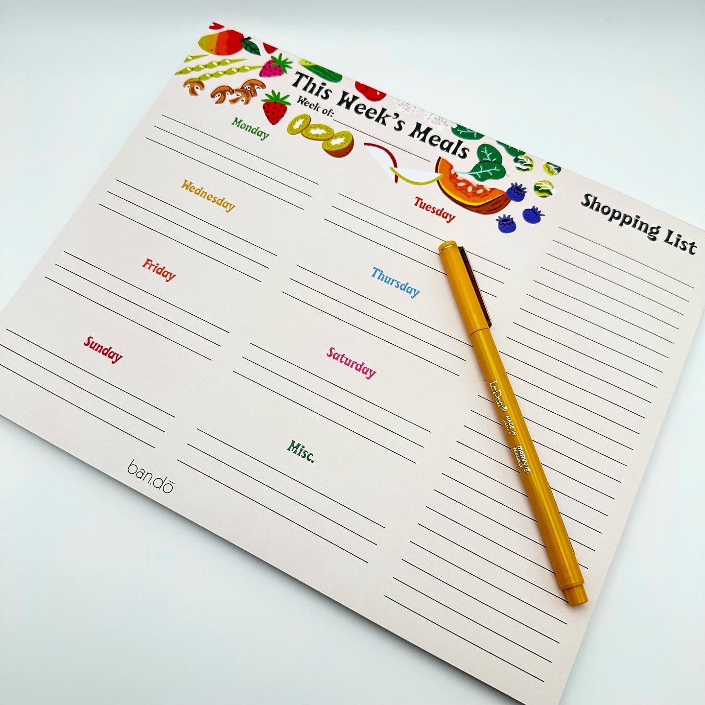 Notepad for weekly meal planning. Has sections for each day, as well as a miscellaneous section and a shopping list you can remove separately to take with you. It is decorated with various fruits and vegetables at the top.