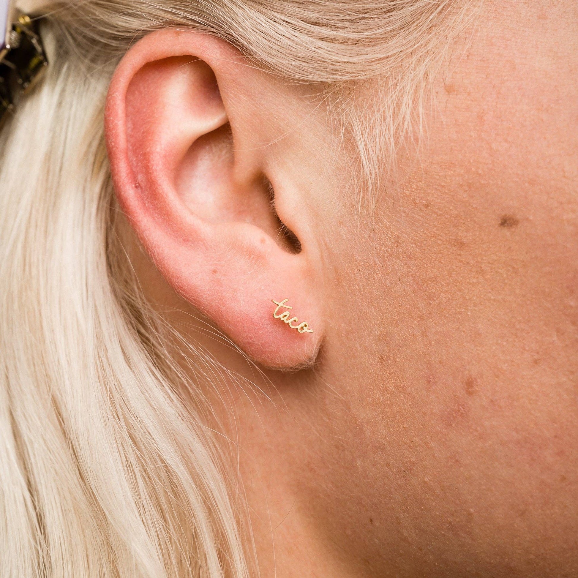 14k gold plated, single stud earring in script text that reads "taco" -- worn on ear 
