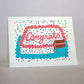 Congrats sheet cake card with sprinkles and confetti. The cake has a slice taken out of it to reveal a chocolate cake with pink frosting.