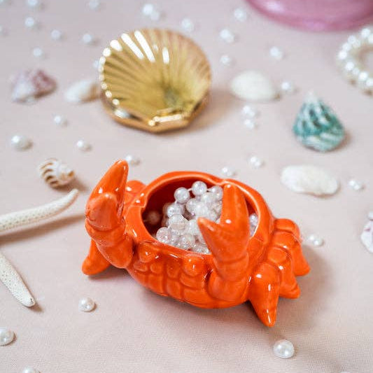 Orange crab-shaped dish with pearls on a pink background with shells and pearls