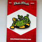 Green pickle cartoon character pin on a red and white card with 'Deli Fresh Threads' branding.