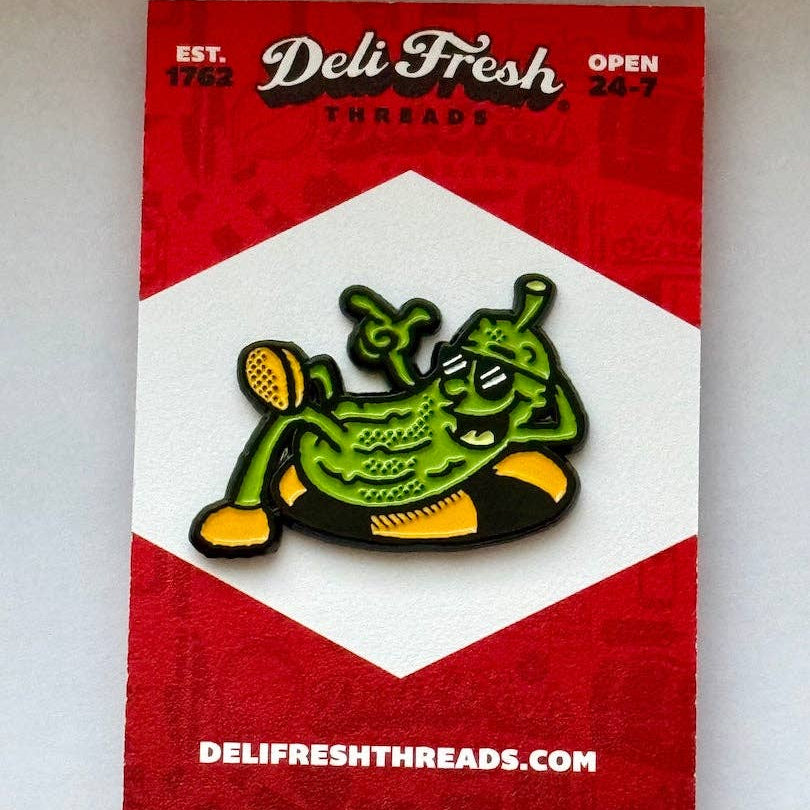 Green pickle cartoon character pin on a red and white card with 'Deli Fresh Threads' branding.