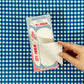 Hand holding a paper milk carton notepad against a blue checkered background