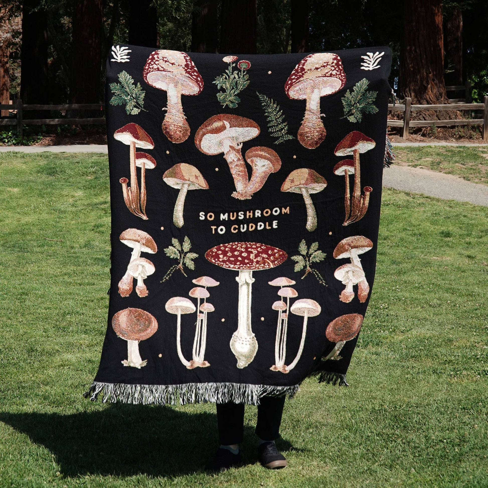 Mushroom throw blanket held up by someone standing on grass 