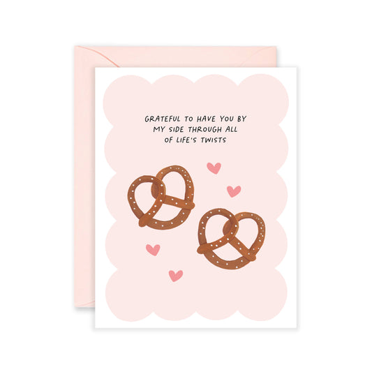 Pink greeting card with two pretzels and some hearts on it with text that reads "grateful to have you by my side through all of life's twists" 