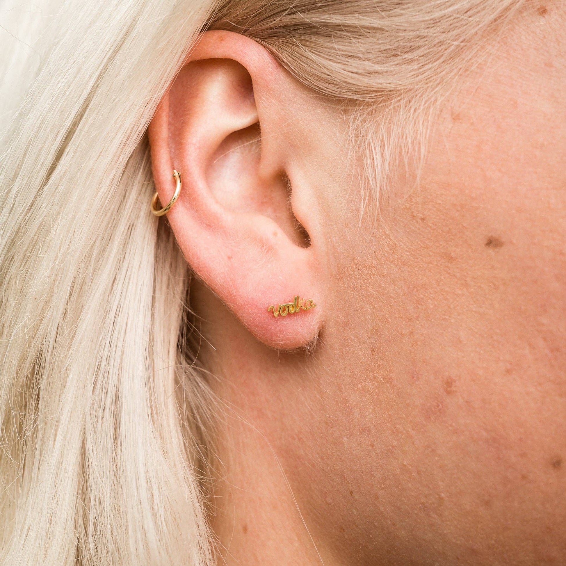 Single 14k gold plated stud earring -- reads "vodka" in handwritten script. Shown on ear for scale 