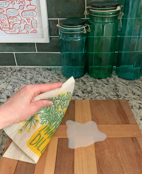 Photo of dill sponge cloth being used to clean up a spill on a cutting board.