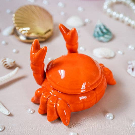 Orange crab-shaped container on a decorative background with pearls and shells